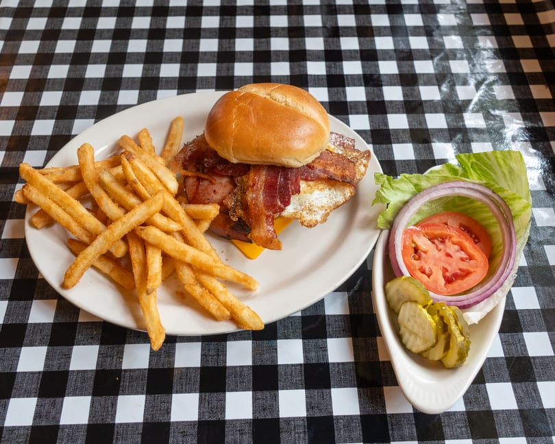 Bacon, egg, and cheese sandwich with golden fries and fresh toppings on a checkered tablecloth.