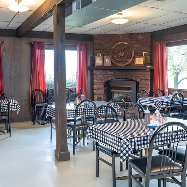 Restaurant dining room with black and white checkered tablecloths, black chairs, and a brick fireplace.