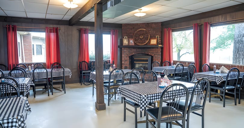 Restaurant dining room with black and white checkered tablecloths, black chairs, and a brick fireplace.