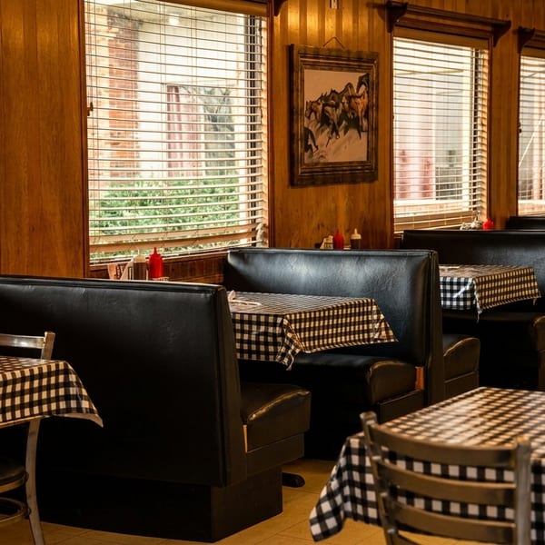 Empty diner interior with black booths, checkered tablecloths, and wooden blinds on windows.