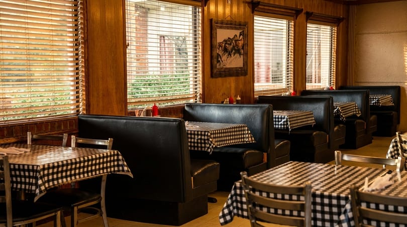 Empty diner interior with black booths, checkered tablecloths, and wooden blinds on windows.