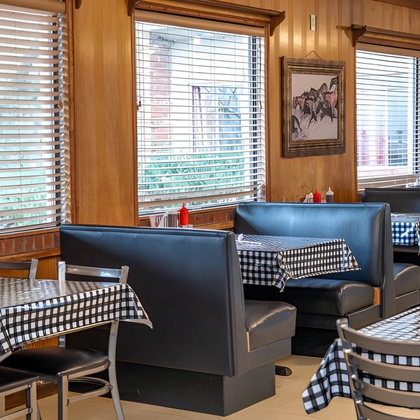 Diner interior with black booths, checkered tablecloths, and wood-paneled walls with window blinds.