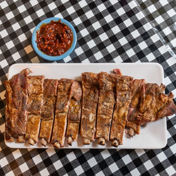 Sliced BBQ ribs and a side of baked beans on a black and white checkered tablecloth.