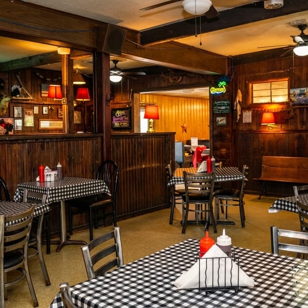 Cozy restaurant interior with checkered tablecloths, wooden walls, and warm lighting from lamps and neon signs.