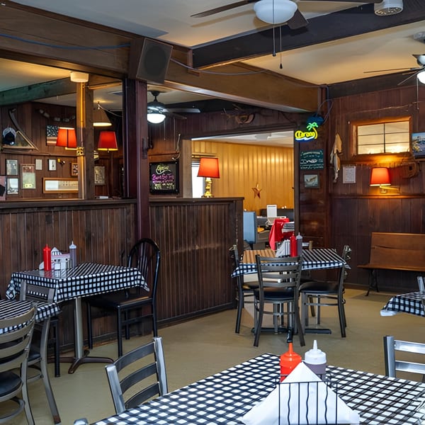Cozy restaurant interior with checkered tablecloths, wood paneling, and neon signs on the walls.